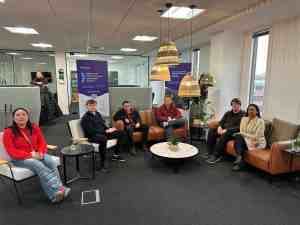 Apprentices sat on office sofas smiling at camera