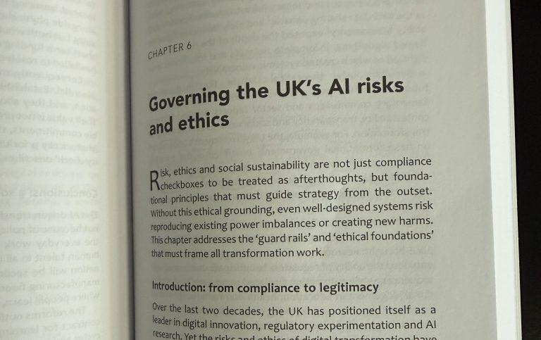 A photograph of an open book showing the start of Chapter 6, titled 'Governing the UK's AI risks and ethics.' The opening paragraph explains that risk, ethics and social sustainability are foundational principles that must guide strategy from the outset, and that the chapter addresses the guard rails and ethical foundations that must frame all transformation work. A subheading reads 'Introduction: from compliance to legitimacy,' with the first lines of that section visible below.